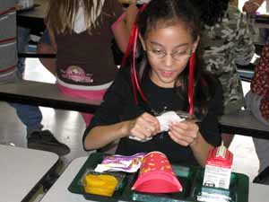Elizabeth in the school cafeteria opening her plastic ware