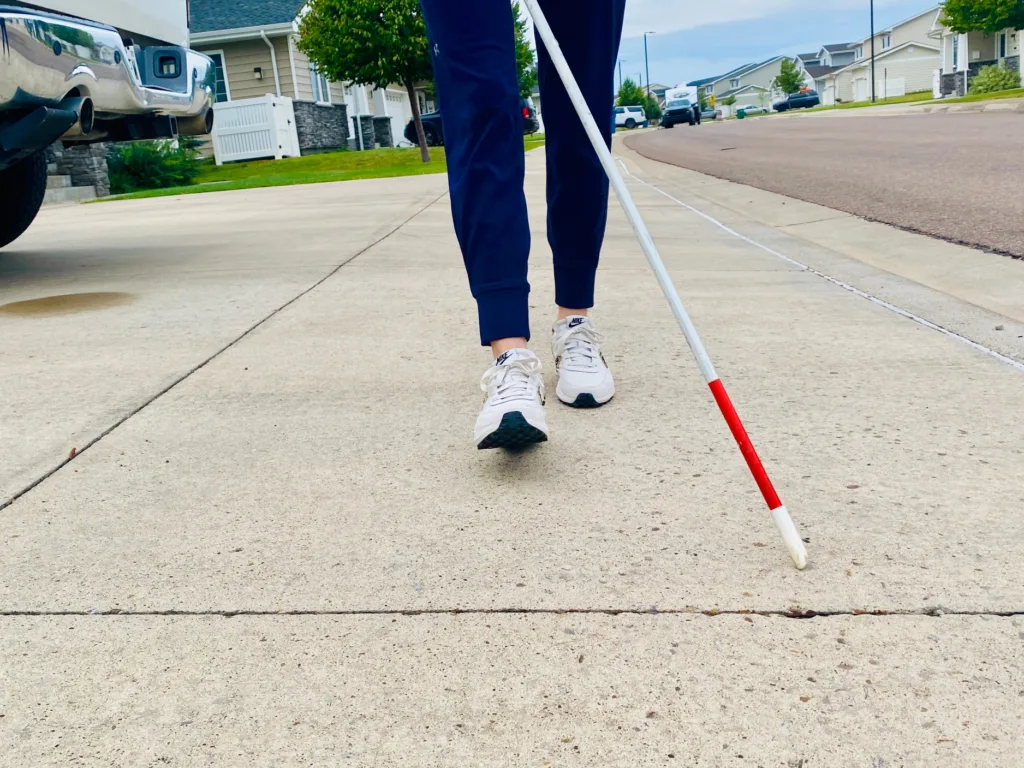 person walking a neighborhood using a white cane