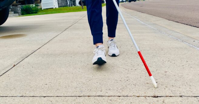 person walking a neighborhood using a white cane