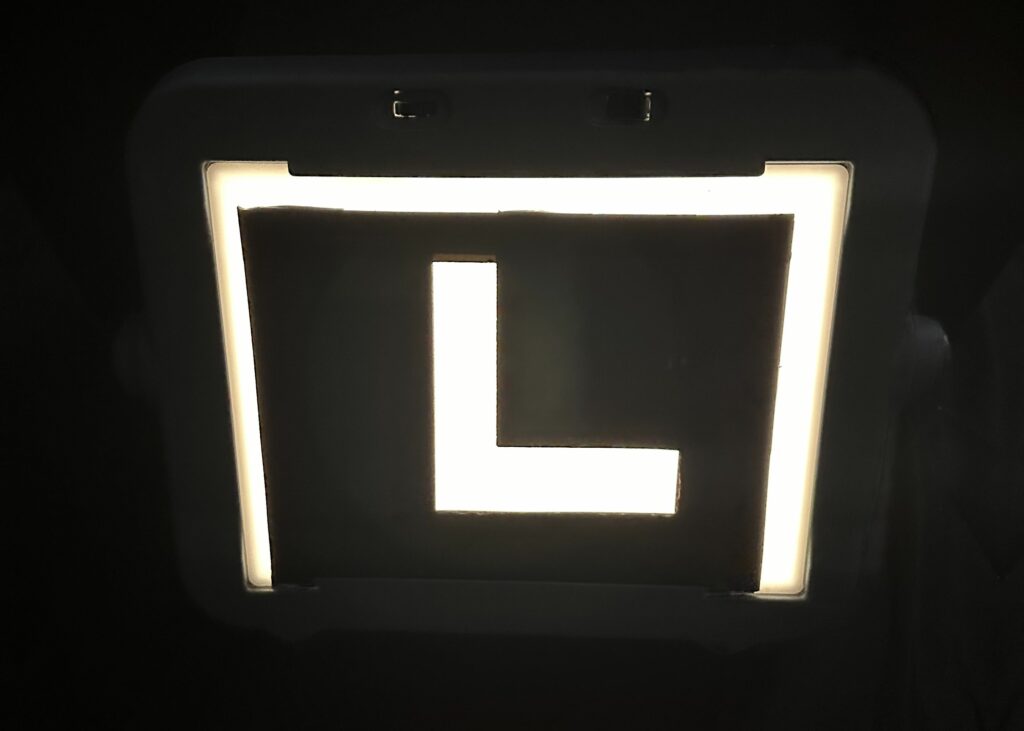 Black outline of the capital letter “L” on a lightbox in a dark room.