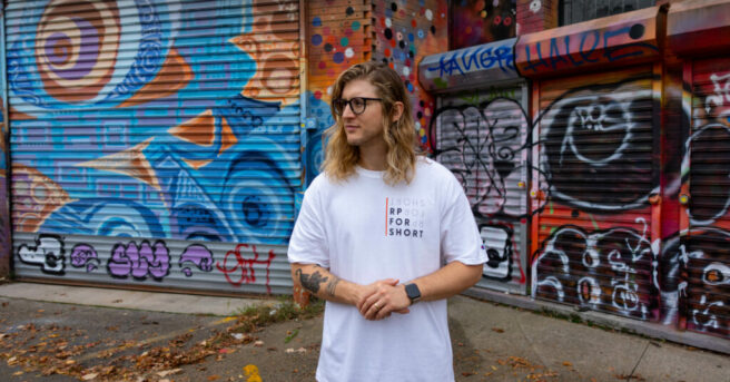 Individual wearing “RP for Short” t-shirt in front of a graffitied wall.