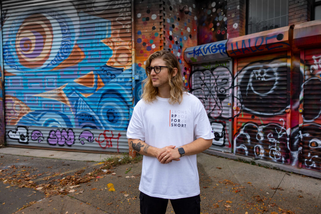 Individual wearing “RP for Short” t-shirt in front of a graffitied wall.