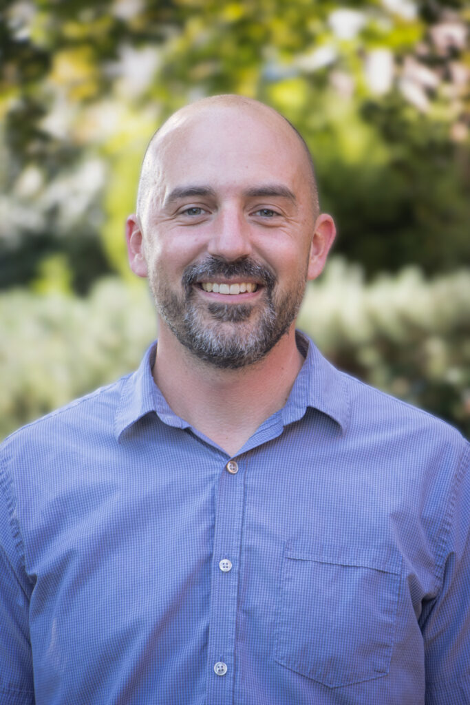 bald man with close cropped dark beard wearing a lavender button down shirt