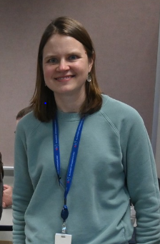smiling woman with should length brown hair wearing light green sweat with blue staff ID lanyard