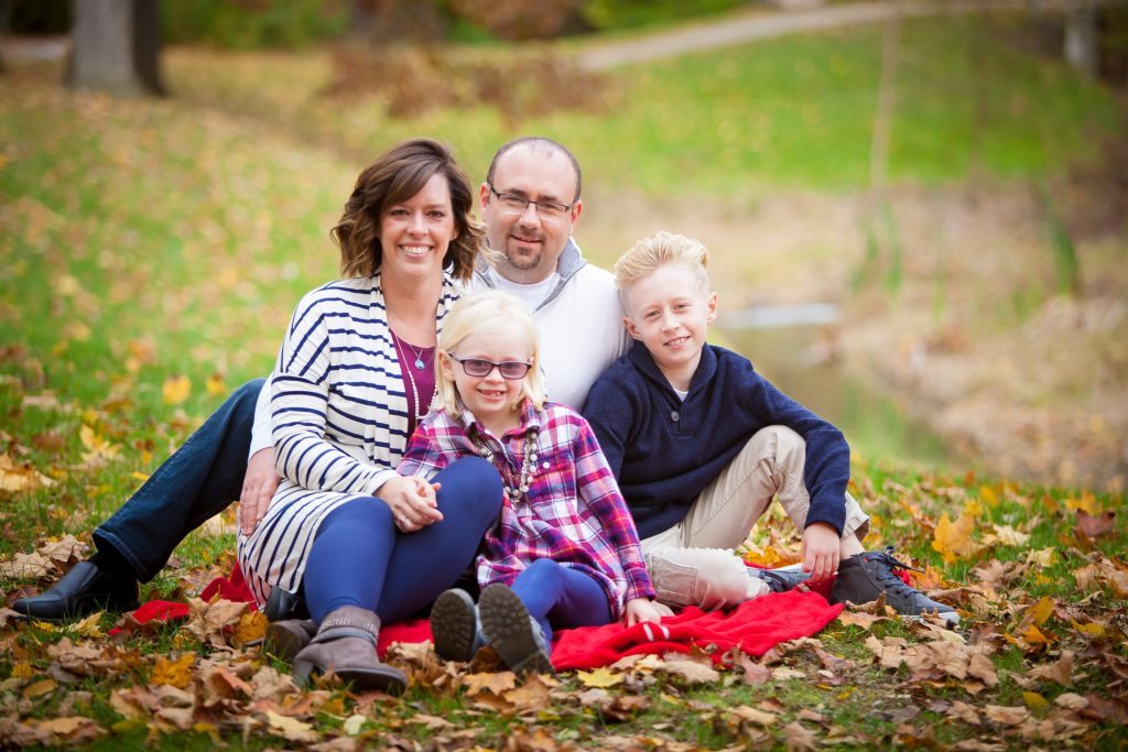 Family portrait of Melissa Mathews, her husband, son and daughter sitting in leaves in a yard