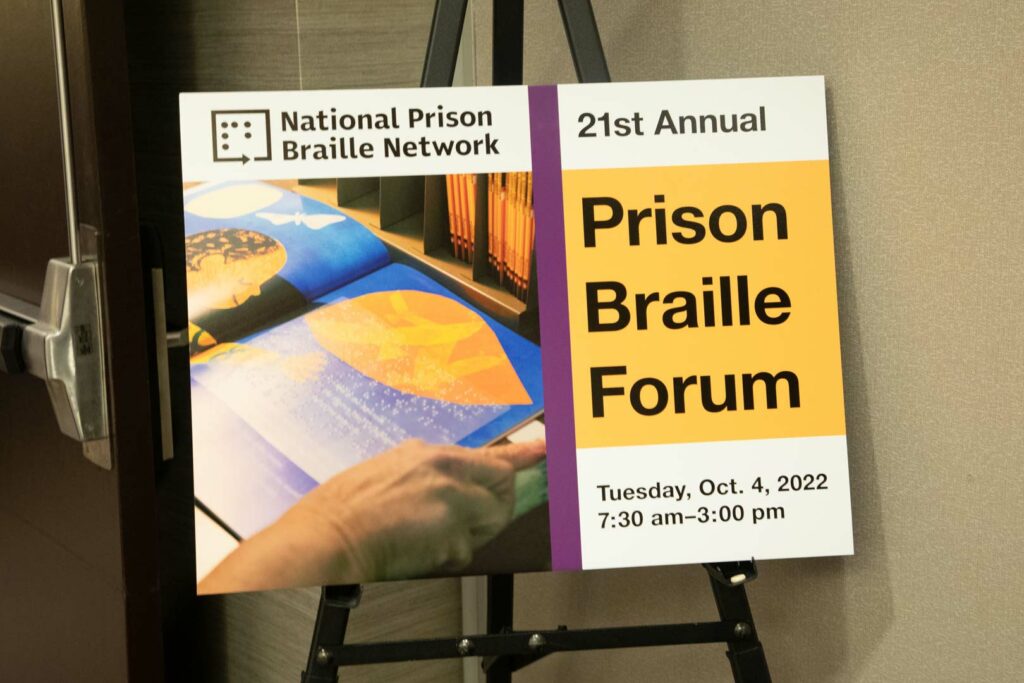 Poster with 21st Annual Prison Braille Forum and image of book with braille sticker placed outside an open door.