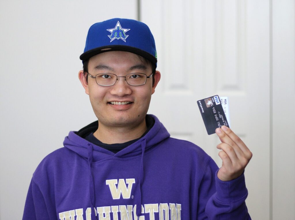 Teen wearing glasses holds two credit cards.