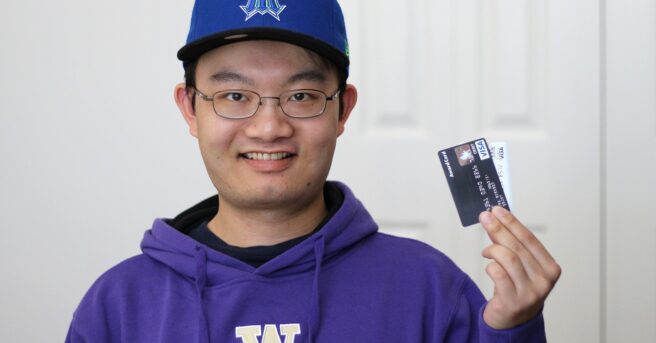 Teen wearing glasses holds two credit cards.