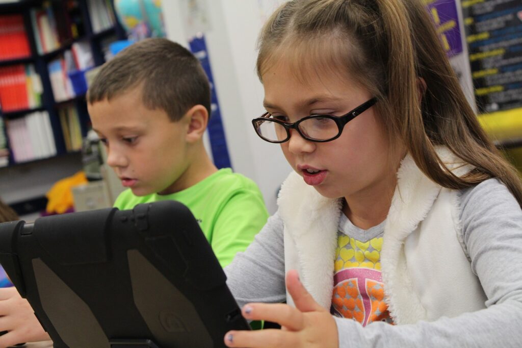 A student wearing glasses uses an iPad in the classroom.