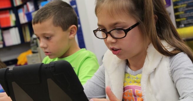 A student wearing glasses uses an iPad in the classroom.