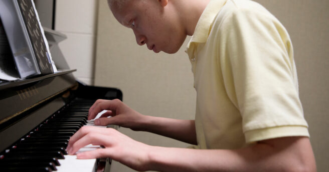 A teenage boy with albinism playing a piano.