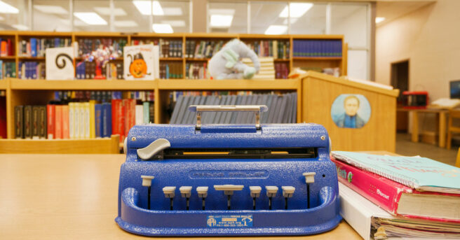 A Perkin's Braille Writer on a bookshelf in a library.