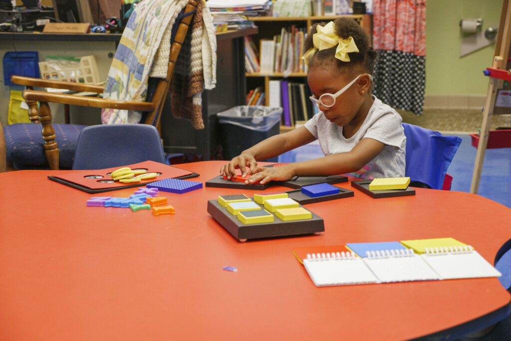 A preschooler sitting at a school table working on tactile puzzles.