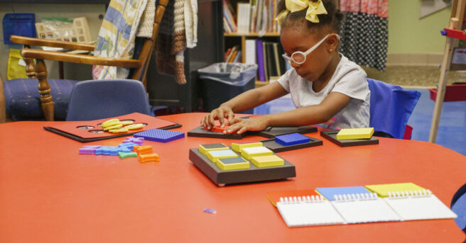 A preschooler sitting at a school table working on tactile puzzles.