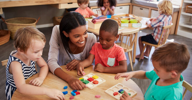 children seating with a teacher around a table playing with manipulatives.