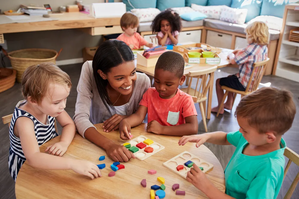 children seating with a teacher around a table playing with manipulatives.