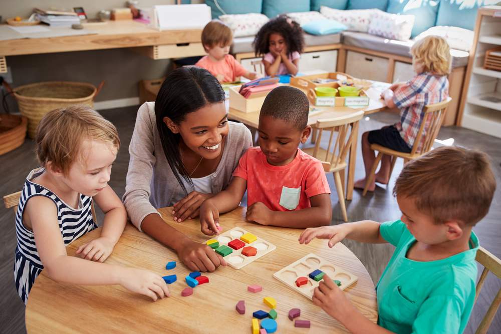 children seating with a teacher around a table playing with manipulatives.