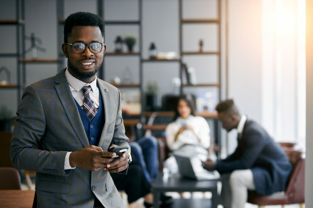 Person in business wear and glasses smiles in an office.