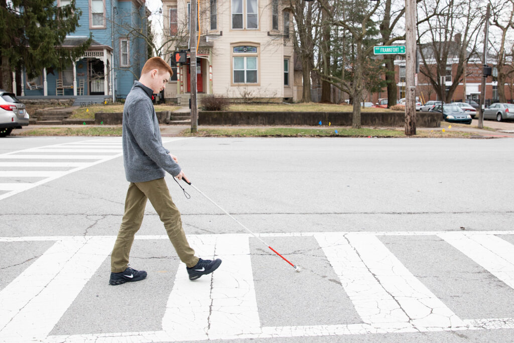 Young man walking on a pedestrian crossing using a white cane