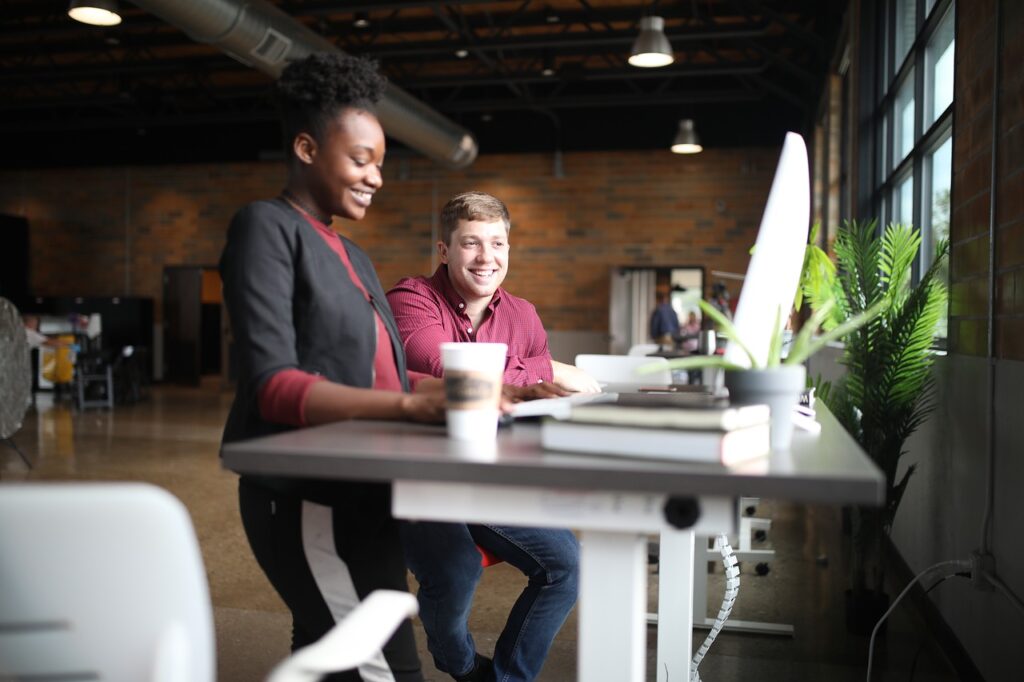 Two coworkers smile and converse at a standing desk.