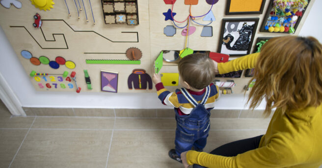 A boy exploring a sensory wall with a paremt