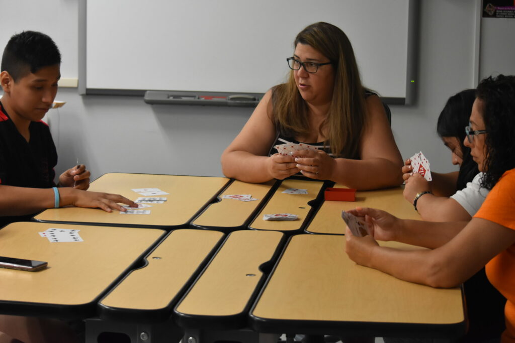 A teacher with several students at desks playing cards with a deck of braille cards.