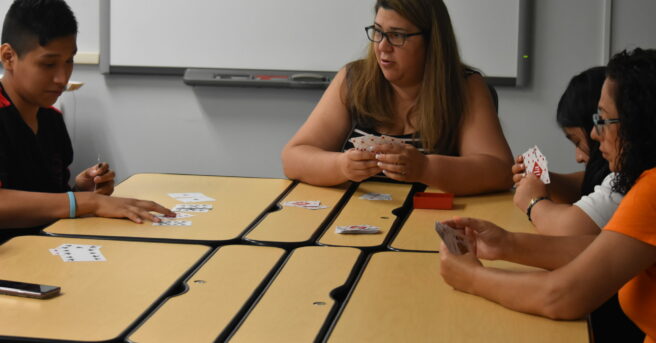 A teacher with several students at desks playing cards with a deck of braille cards.