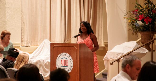 Student speaking from behind a podium to an audience.