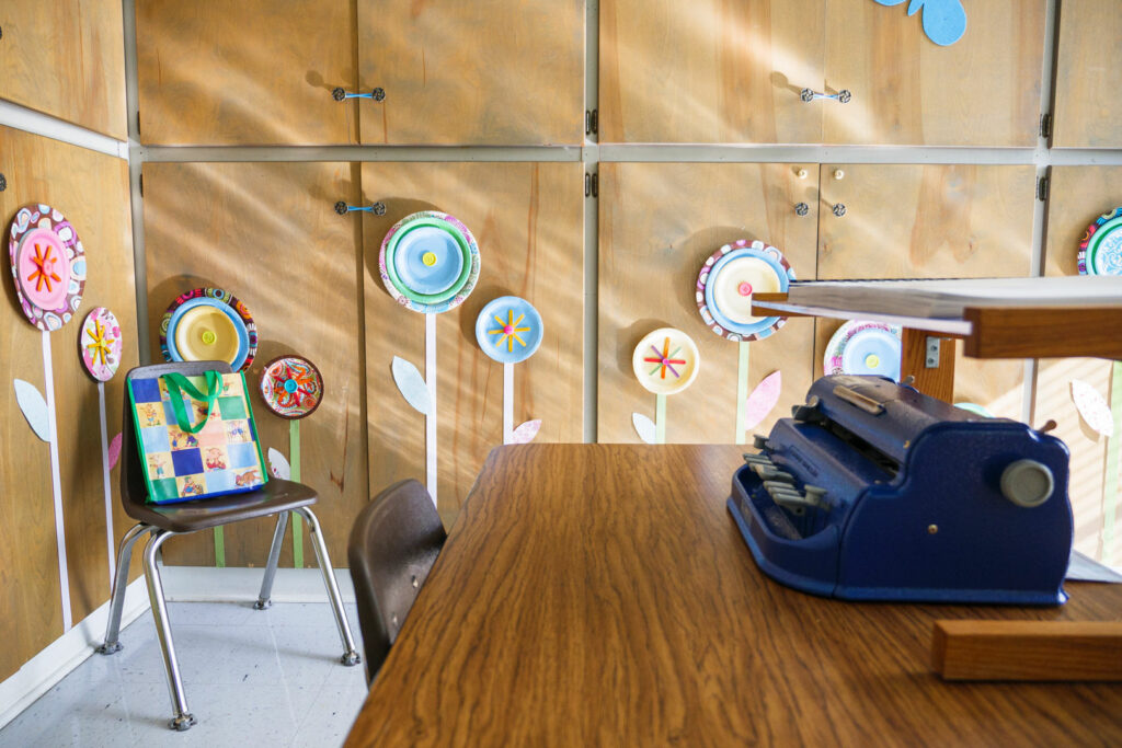 A preschool room with flower art on the wall and a Perkin's Braille Writer on a desk.