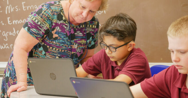 A teacher working with a student at his desk on his computer.