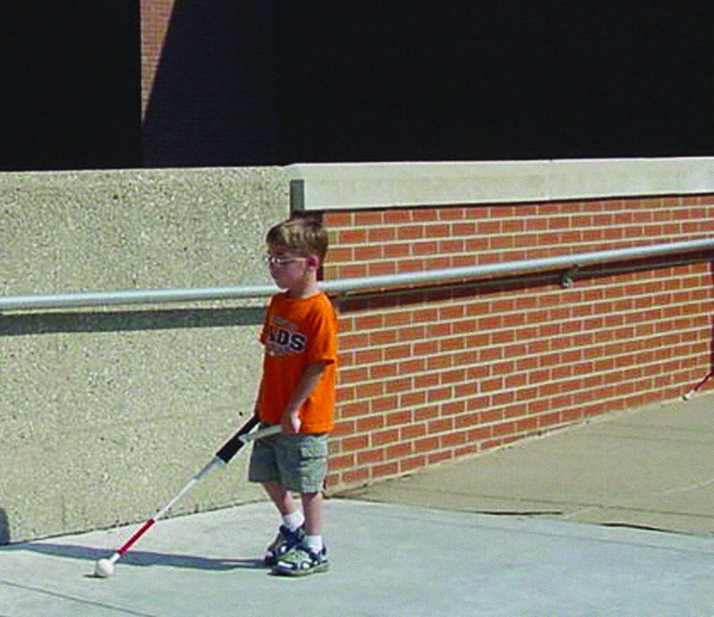 Young boy walking outside with a white cane.
