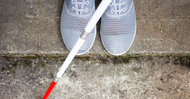 White shoes on a sidewalk with a cane in front of them.