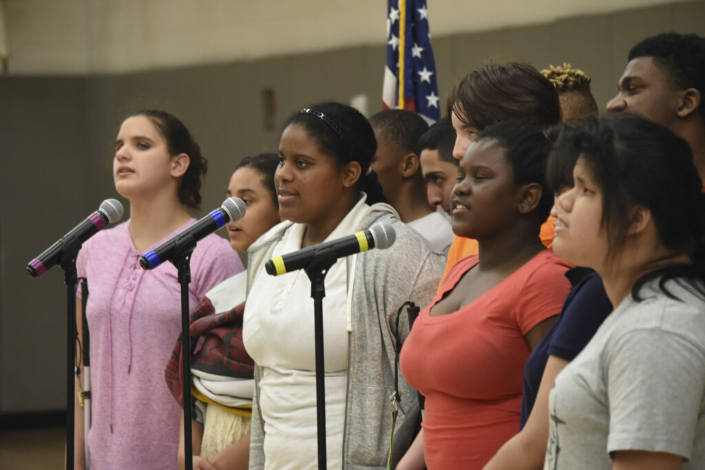 A group of teens singing into microphones.