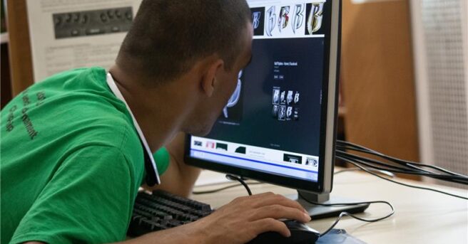 A college student sitting at a table using a computer with magnification and leaning into the screen.