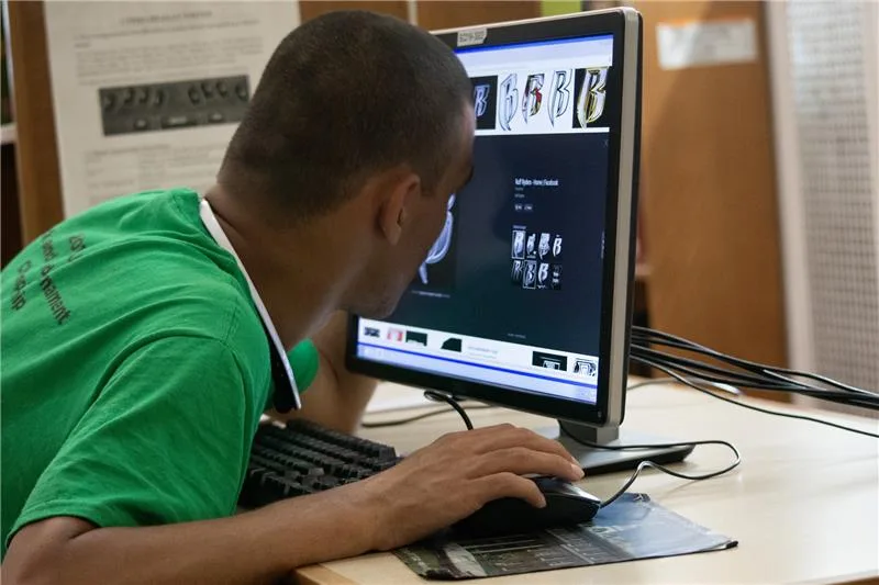 A college student sitting at a table using a computer with magnification and leaning into the screen.