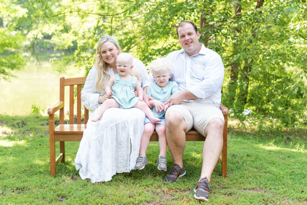 Family with two small children with fair skin and hair sit on bench and smile