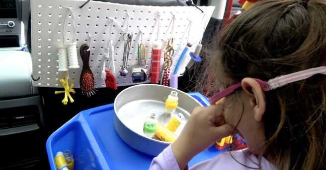 A child sitting in the back seat with various activities attached to the back of the passenger seat and the handle above the window.