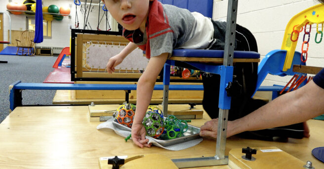 Child on a support bench kicking chimes with their feet.