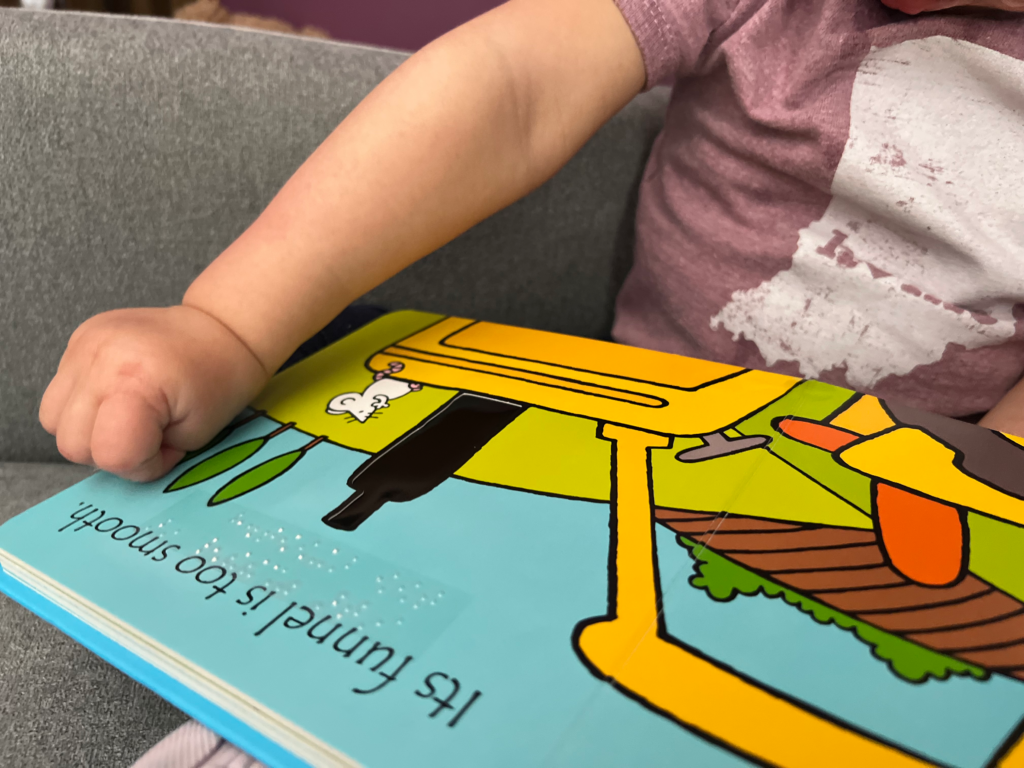 Touch and feel Board book with braille and a young child feeling the page.