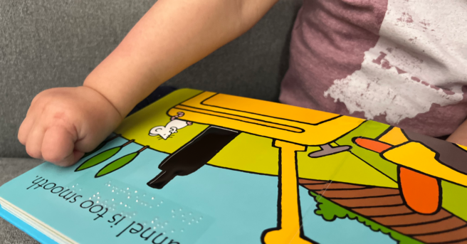 Touch and feel Board book with braille and a young child feeling the page.