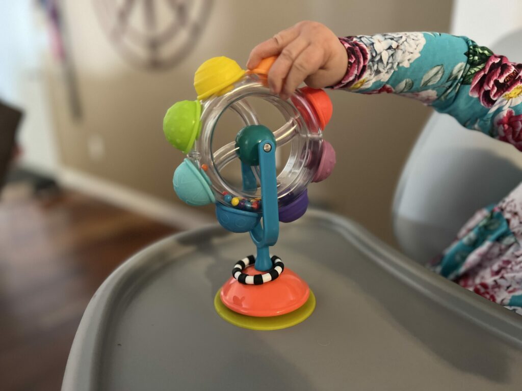A spinner toy suctioned to a high chair as a child is playing.