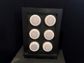 enlarged representation of a braille cell created using a small black chalkboard stand and six circular tap lights. It sits on a black box, and a black trifold board sits behind it.