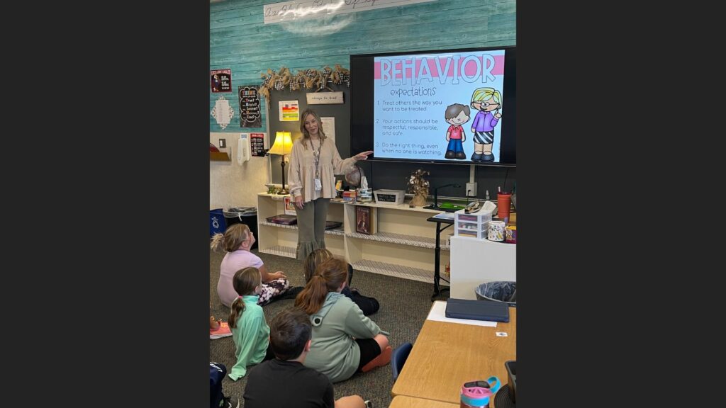 A teacher pointing to her smart board with a list of behavior expectations.