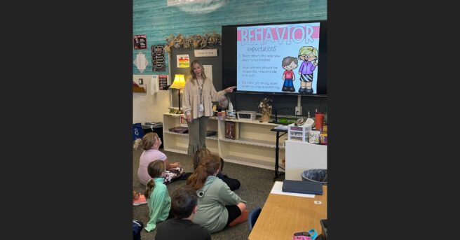 A teacher pointing to her smart board with a list of behavior expectations.