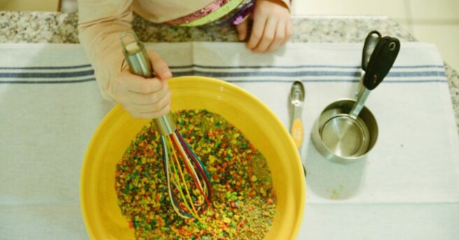 image of a child using a whisk to stir a bowl of brightly colored pulverized cereal.