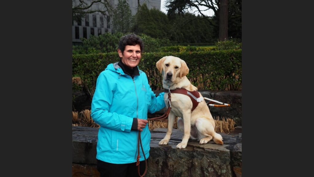 Adult smiling outdoors with a dog guide in harness.