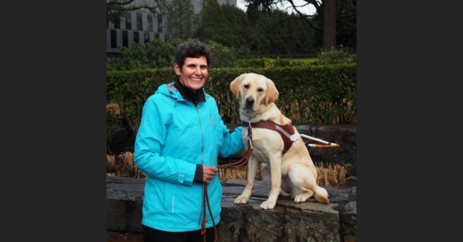 Adult smiling outdoors with a dog guide in harness.