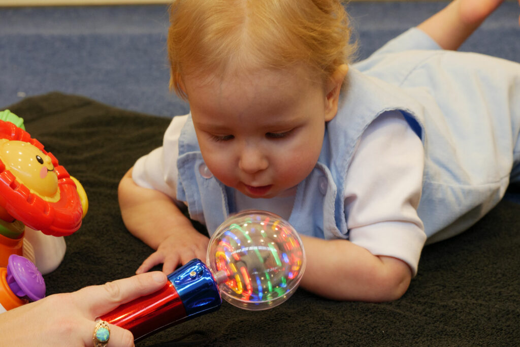 A baby on a black towel reaching and engaging with a light up toy.