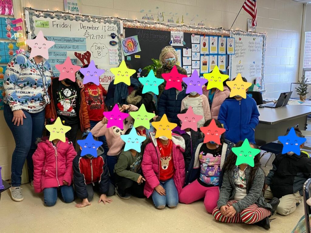 Young adult stands in a classroom surrounded by elementary students (whose faces are covered by stars for privacy)