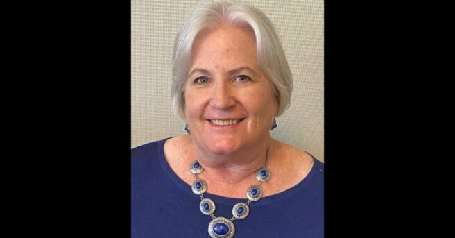 Headshot of Zelda Gebhard wearing a blue shirt and bold necklace.